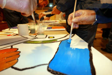 Mitarbeitende malen gemeinsam an einem Firmenkunstwerk im Teambuilding Workshop